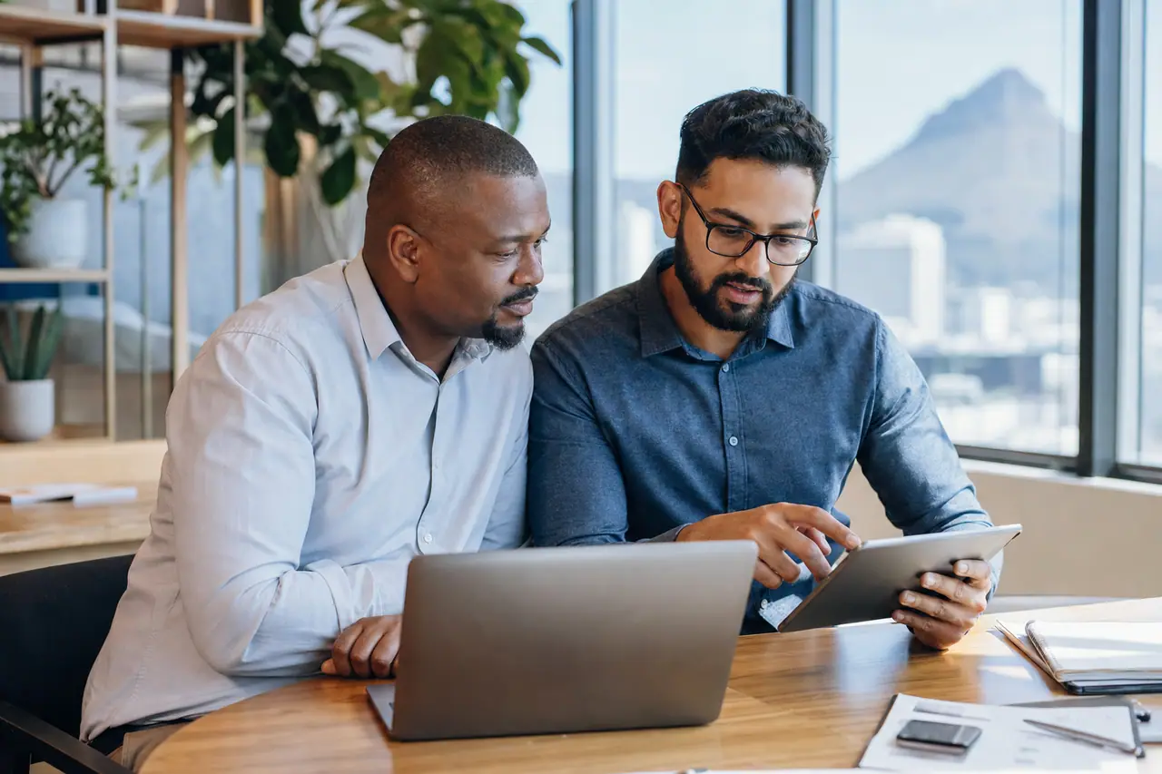 South African business client and software consultant reviewing a custom application on a laptop and tablet